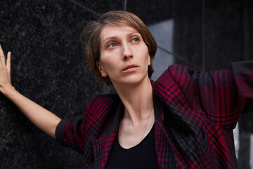 melancholic lonely young woman with short hair in red checkered jacket outdoors in front of building. portrait of caucasian female