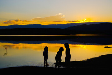 Fototapeta premium Silhouettes of happy children playing on the lake at the sunset time, Reservoir Amphoe Wang Saphung Loei Thailand
