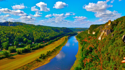 Elbe passing though Saxon Switzerland seen from uphill vista. The river reflects beautiful deep blue sky with white clouds.