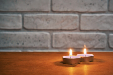 Fototapeta na wymiar Two burning candles on the table against the background of the wall