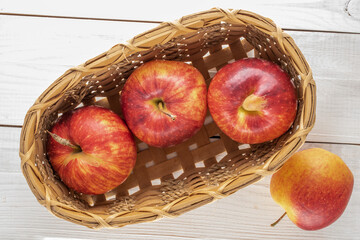 Several organic red apples with a basket on a wooden table, close-up, top view.