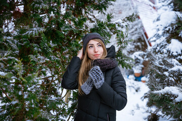 Beautiful smiling young woman in winter outdoors in warm jacket enjoys weather among the snow-covered trees. Caucasian girl on a walk in winter. Winter concept