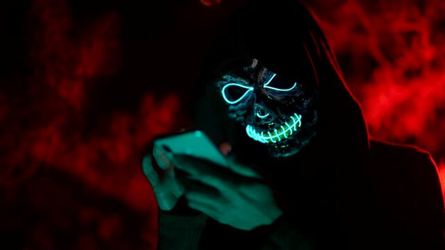 Creepy portrait of a man in a death mask at night with a phone typing a message
