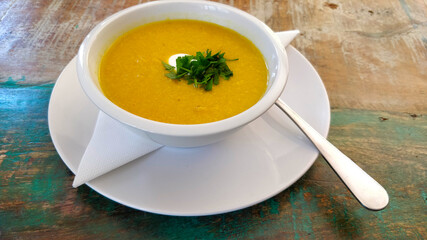 Delicious pumpkin cream soup in ceramic cup on old fashioned table viewed from top.