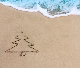 Christmas background with fir tree drawing in the sand at the caribbean beach.