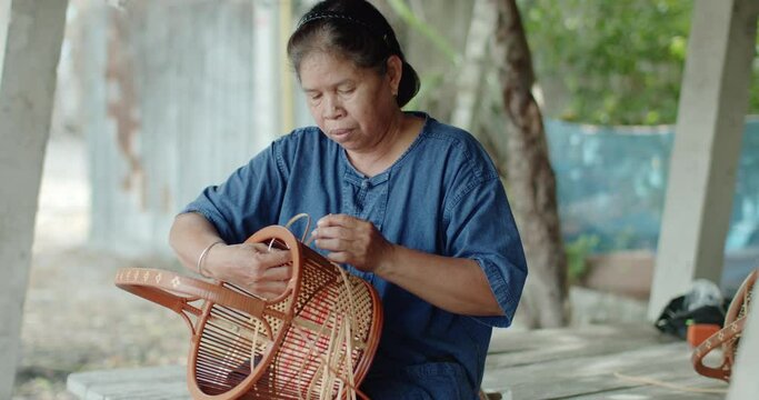 Cut in shot of Thai female farmer weave basket in traditional Thai art patterns to sell as extra income in countryside of Thailand	