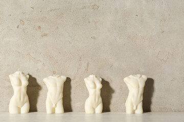 Beautiful female and male body shaped candles on table near light wall