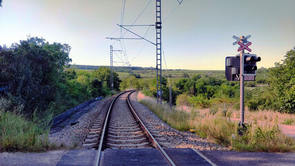 Fototapeta na wymiar Railroad goes through the beautiful nature of South Moravia. The track is lined with electric power poles. The viewer stands on road crossing. Weather is very nice and pleasant. Surrounding bushes and