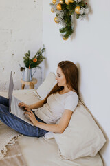 A beautiful woman working remotely at home takes notes on a computer while sitting on a bed