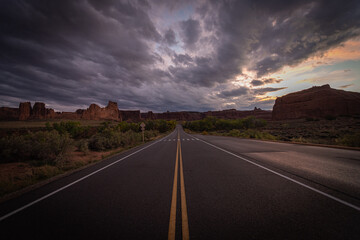 Long desert road in the middle of nowhere under moody dramatic stormy sunset sky