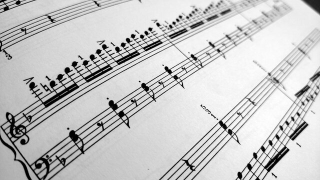 Detail view on music sheet with black notes on the white paper. The sheet is written for piano.