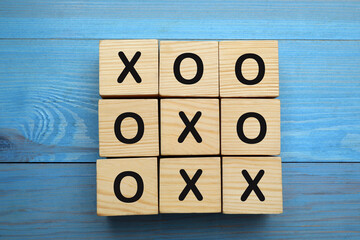Tic tac toe cube set on light blue wooden table, flat lay