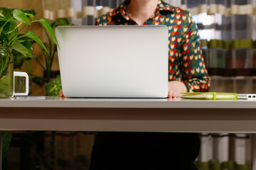 Unrecognizable woman with working on computer at home. Start or finish of a work day. Young woman seating at the working table and laptop. Workplace. Female hand. Green notebook, plant. Copy space