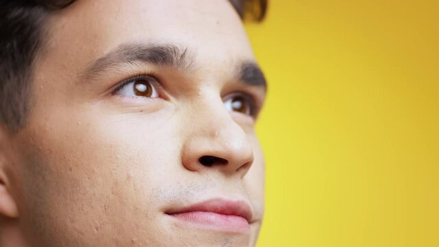 Extreme close up portrait of young inspired caucasian man looking up with delight and smiling, empty space, slow motion