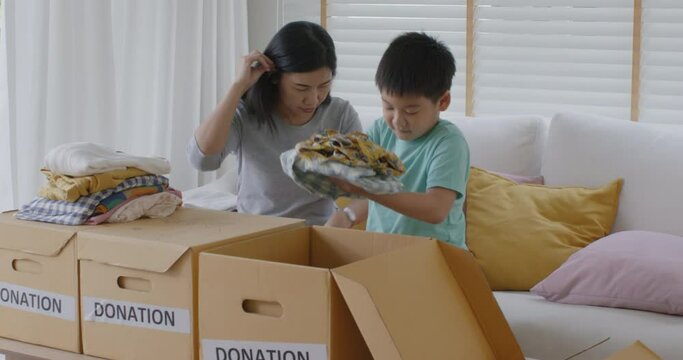 Small gift donate for social issue relief alms unity care at home. Asia little boy kid son and mom smile fun help poor people by reuse old used clean clear closet sort stack box zero waste eco saving.