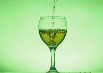 A drink (juice, cocktail, wine) is poured into a glass glass. Photo on a green background.