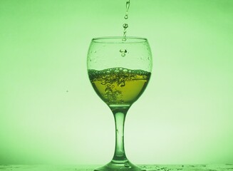 A drink (juice, cocktail, wine) is poured into a glass glass. Photo on a green background.
