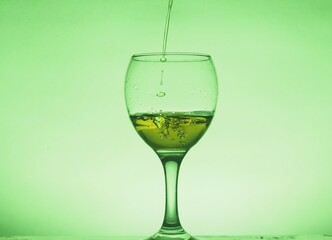 A drink (juice, cocktail, wine) is poured into a glass glass. Photo on a green background.