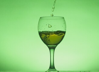 A drink (juice, cocktail, wine) is poured into a glass glass. Photo on a green background.