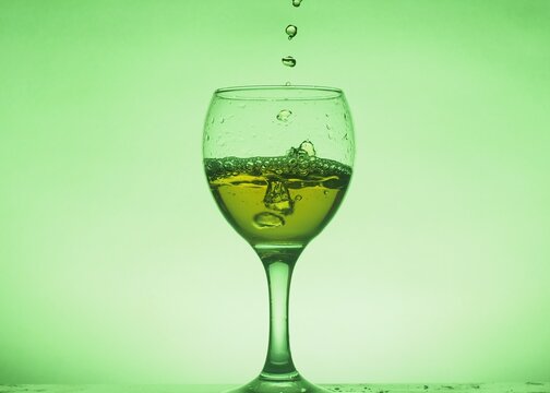A drink (juice, cocktail, wine) is poured into a glass glass. Photo on a green background.