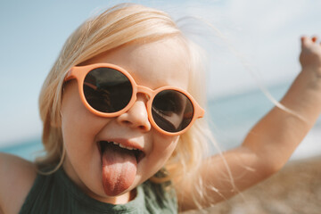Funny kid sticking out tongue playing outdoor happy emotional child in sunglasses 3 years old baby...