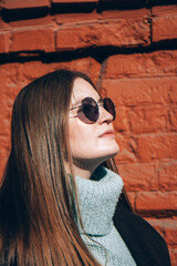 Beautiful woman with long hair in a dark coat walks down the street. Close up. Bright orange wall background