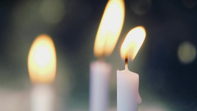 White burning candle flames flickering in the wind against a dark background, creating a spiritual, memorial, and peaceful atmosphere of remembrance and meditation