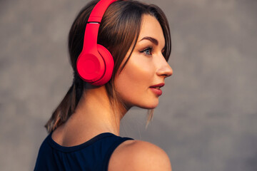 sporty woman, wearing wireless headphones, listening to music and smiling, posing against gray...