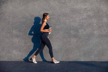 Young sportive woman jumping and running on gray background, female model in sportswear exercising...