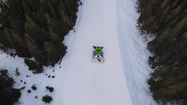 Aerial view of snow groomer preparing the snow on a ski slope at a Swedish ski resort. Snowcat on a snowy mountain. 4K drone footage.