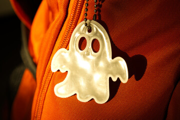 Elegant white reflective safety signal in a ghost pattern form on an orange backpack for pedestrian...