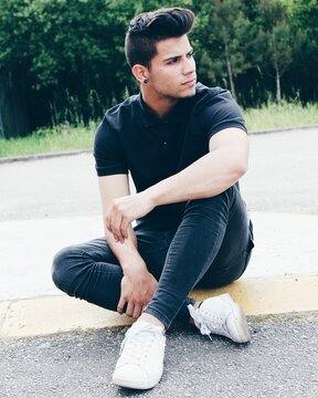 Man In Dark Polo Shirt And Blue Denim Jeans Sitting On Gray Concrete Road