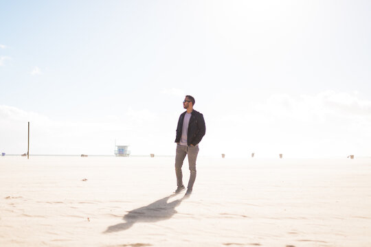 Man in leather jacket looking away standing on sand outdoor