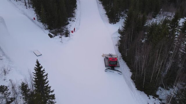 Aerial view of snow groomer preparing the snow on a ski slope at a Swedish ski resort. Snowcat on a snowy mountain. 4K drone footage.