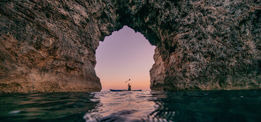 One person on paddle under huge rock