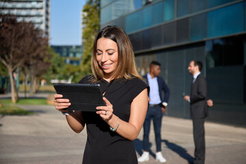 businesswoman looking at data on a tablet outdoors with colleagues in the background