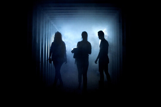 Silhouette of three people in a dark misty underground corridor