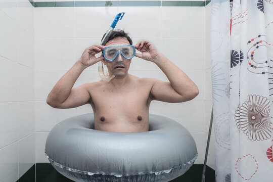Topless man wearing blue goggles on gray inflatable ring standing in the bathroom