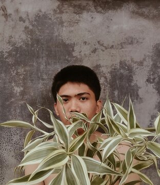 Topless teenage boy standing behind green plant