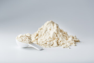 A pile of protein powder with a measuring spoon on a white background. - obrazy, fototapety, plakaty