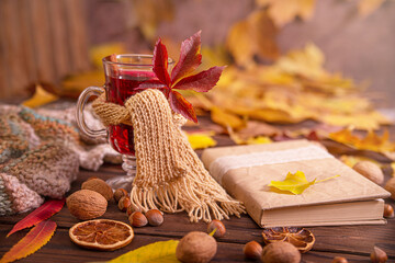Autumn, fall leaves, a glass of hot wine wrapped in a warm scarf on a wooden table background, copy...