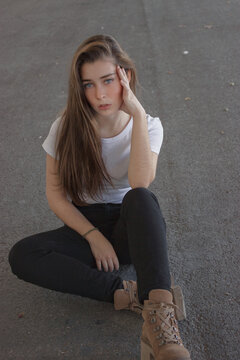 Woman in light shirt and dark pants sitting on gray concrete floor