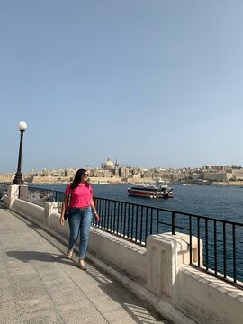 Woman in pink with sunglasses walking by waterside