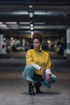 Woman in yellow sweater crouching ion floor in parking lot