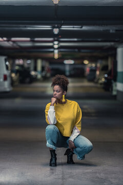 Woman in yellow sweater crouching ion floor in parking lot