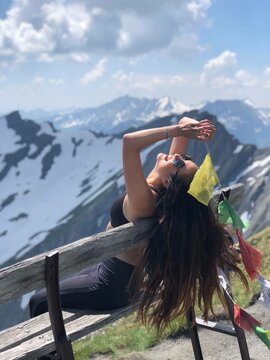 Woman sitting on bench tilting her head backwards and holding buntings near glacier mountains