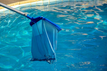 Cleaning pool from garbage with special net. Clear water with blue tint. Concept of hygiene and healthy lifestyle. Horizontal photo. Copy space. Close-up. Selective focus.