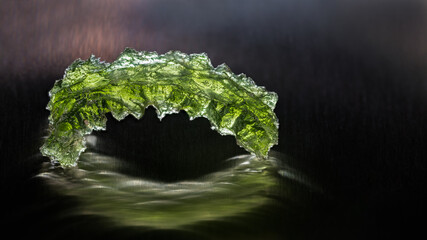 Green moldavite jewel in arch shape on black background with beautiful reflection and mystery glow....