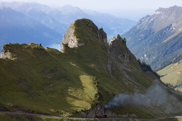 Amazing hiking day in the alps of Switzerland. A beautiful locomotive drives on to a mountain and a lot of smoke comes out of the locomotive. What a view in the background.