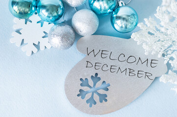 Welcome December, the inscription on a wooden toy in the shape of a mittens next to a new ball and snowflake, festive background